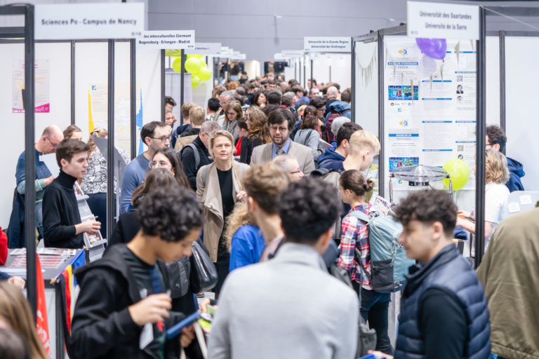 Rechts und links sind Messestände des Deutsch-Französischen Forums zu sehen, dazwischen bewegen sich zahlreiche Besucher*innen.